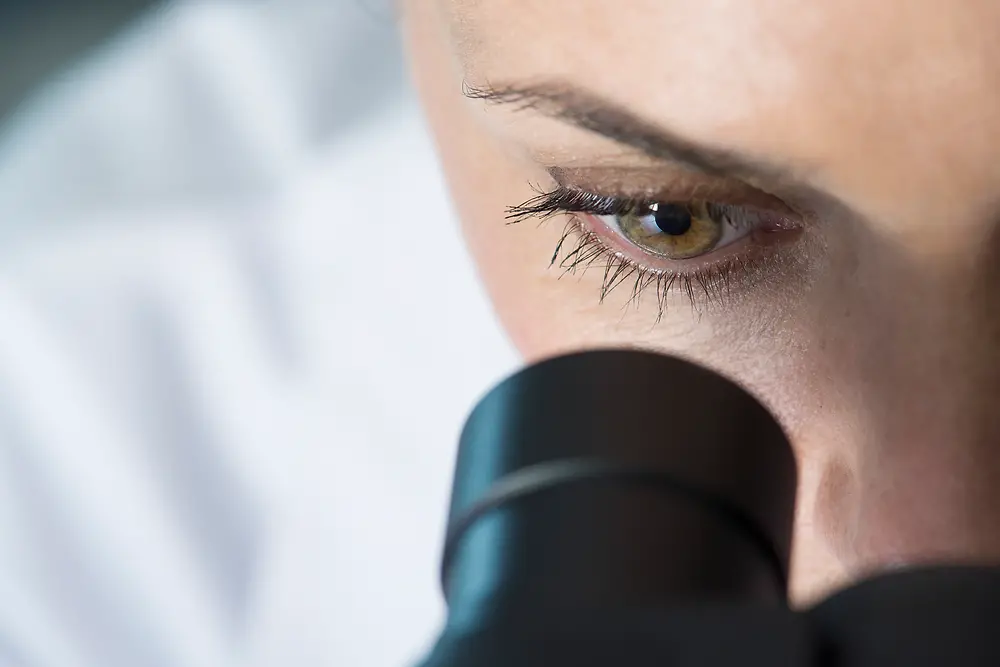 око жінки, яка дивиться у мікроскоп