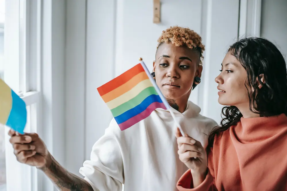 Дві жінки розмовляють між собою, тримаючи в руках прапор ЛГБТК+.