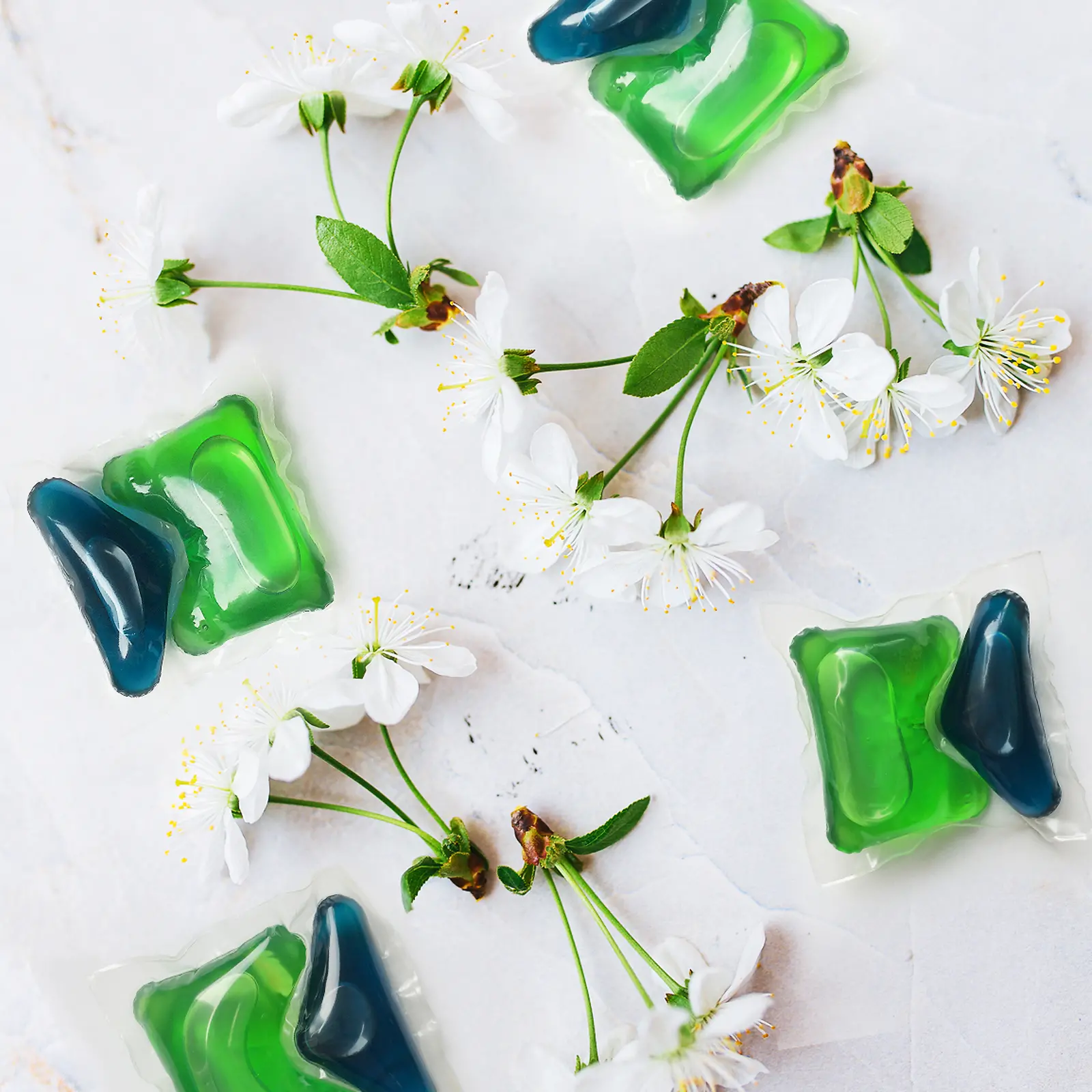 Дві зелено-сині таблетки Henkel Persil із цвітом вишні навколо 