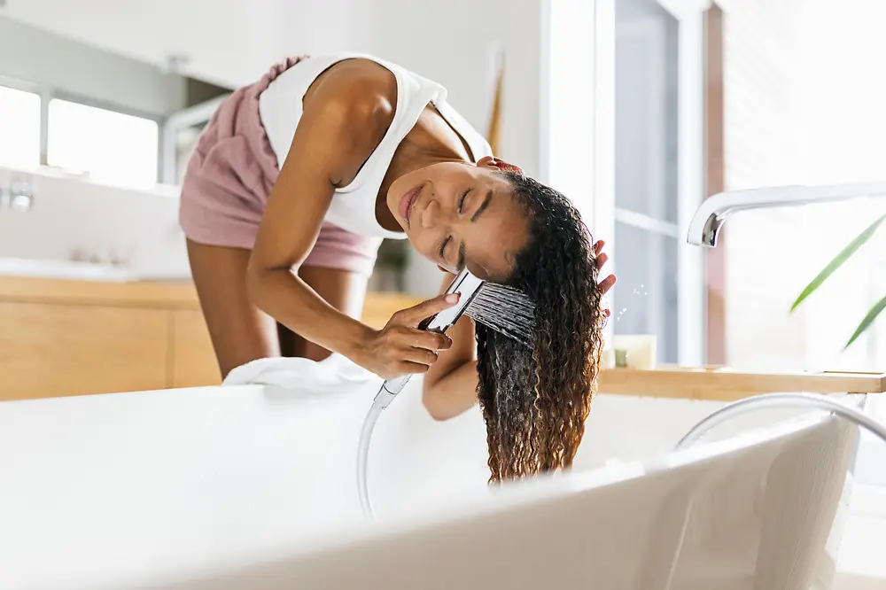 Жінка у ванній кімнаті миє своє довге каштанове волосся 